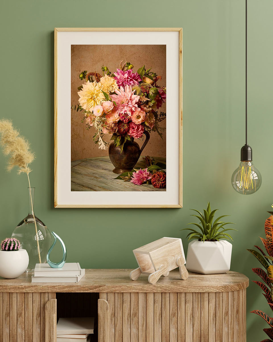 Image of the same floral bouquet with a white mat border, a light wood frame on a green wall in an office