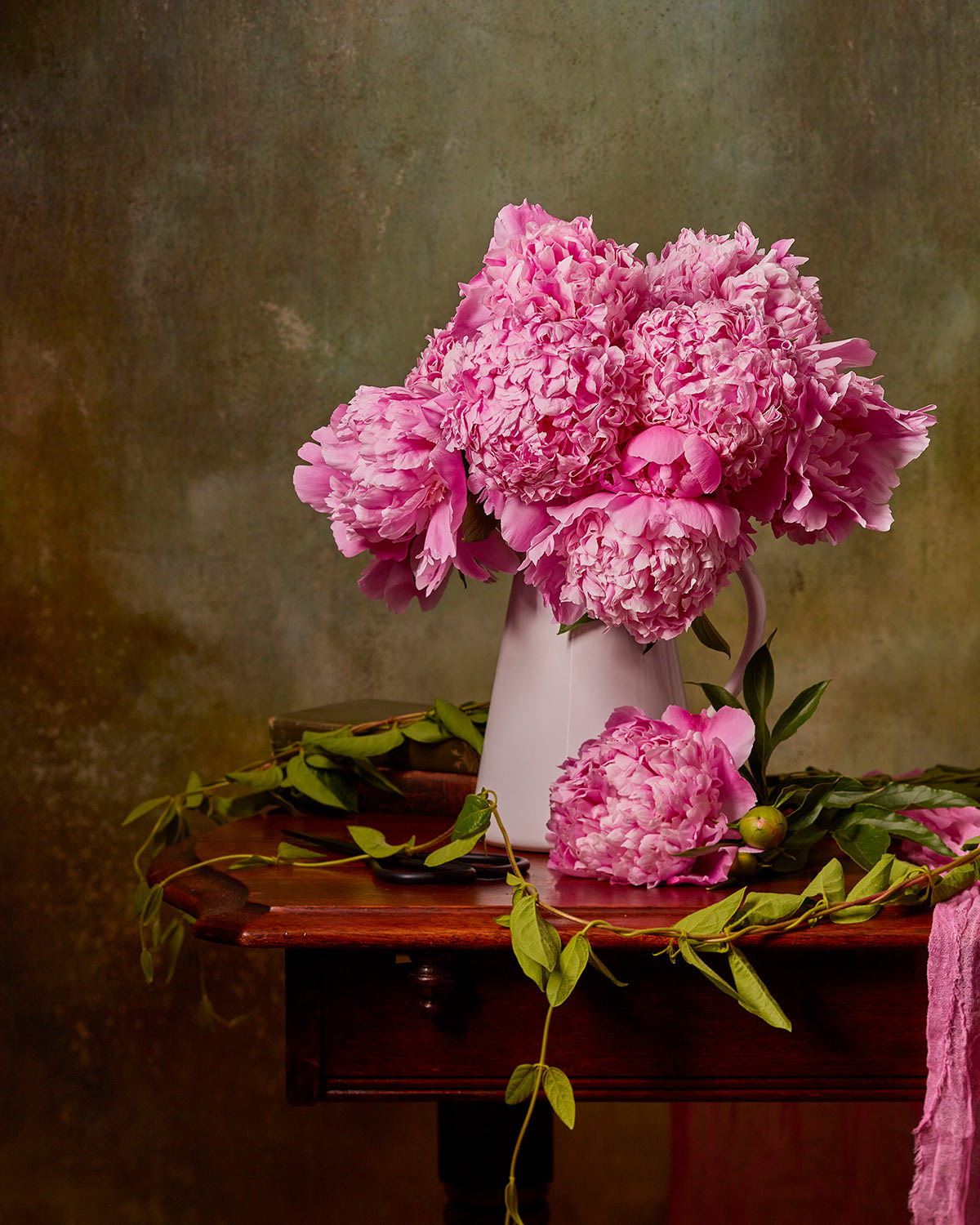 Image several Sarah Bernhardt peonies in a white pitcher on a wood table in a studio environment