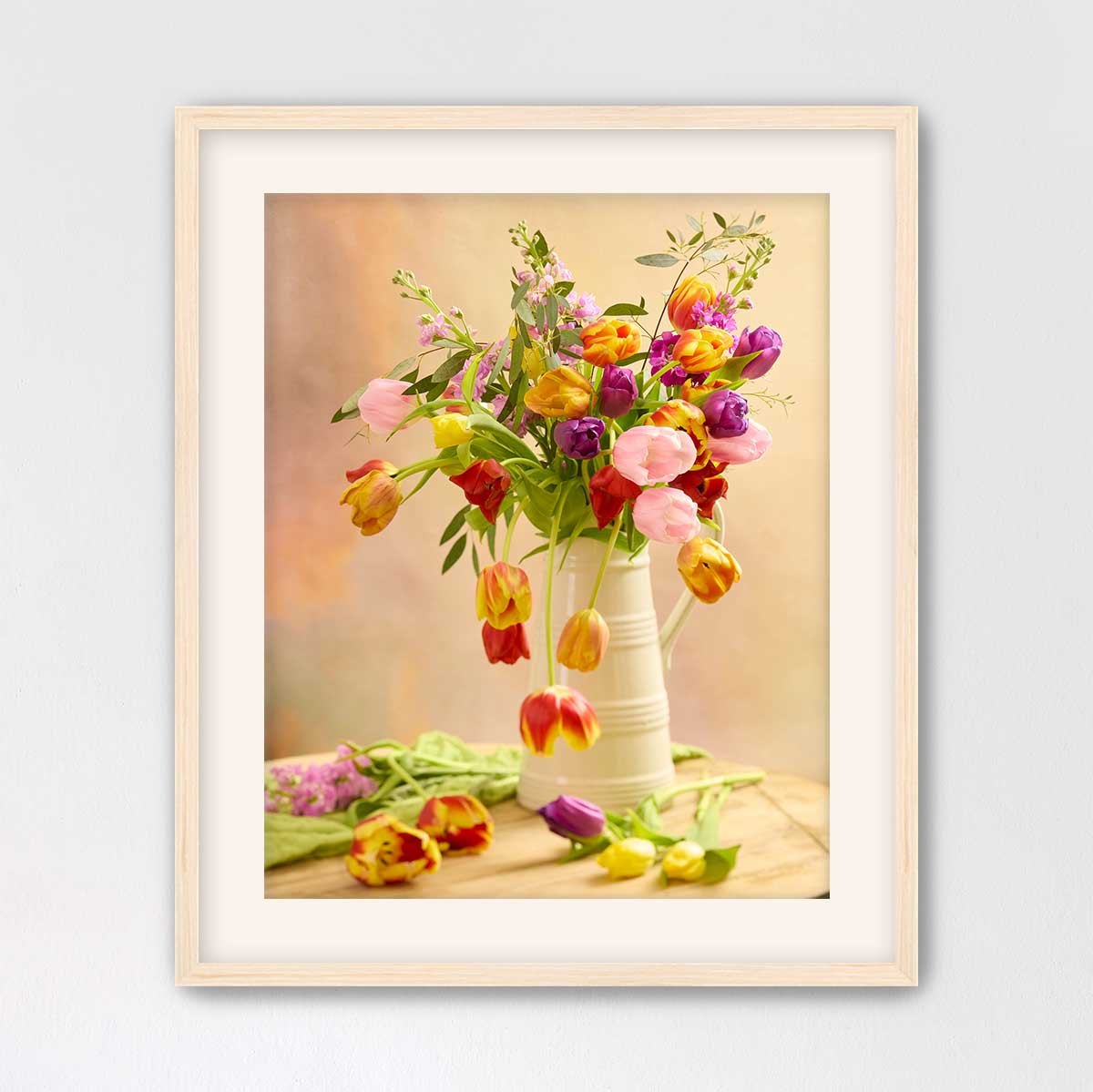 A white vase filled with a vibrant bouquet of tulips in various colors, including red, yellow, pink, and purple, sits on a wooden surface.