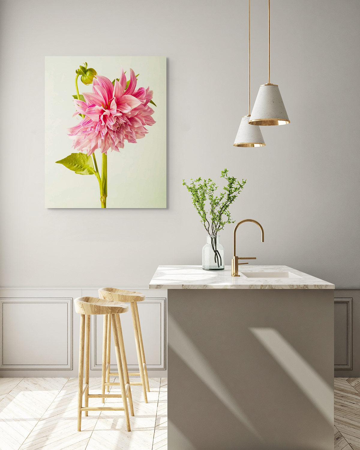 A modern kitchen showcases a marble island with two wooden stools, a vase of green branches, and pendant lights. The Budding Beauty Dahlia canvas wall art injects color into the beige and neutral-toned minimalist space.