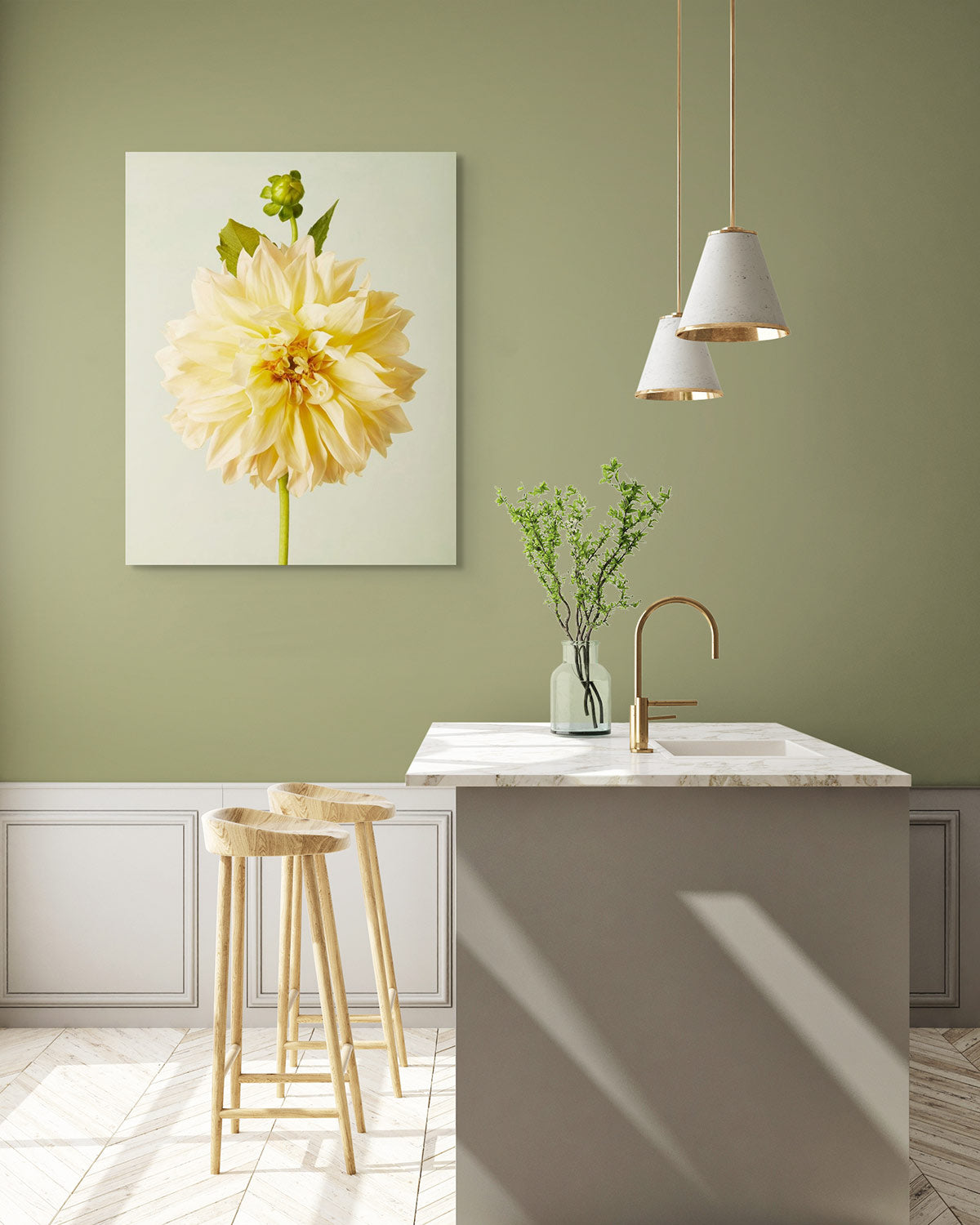 The minimalist kitchen, with green walls, features a fine art giclee of Champagne Petals. A sleek island with a marble countertop and a Café au Lait dahlia vase adds elegance. Wooden stools stand beside it under pendant lights that illuminate the space.