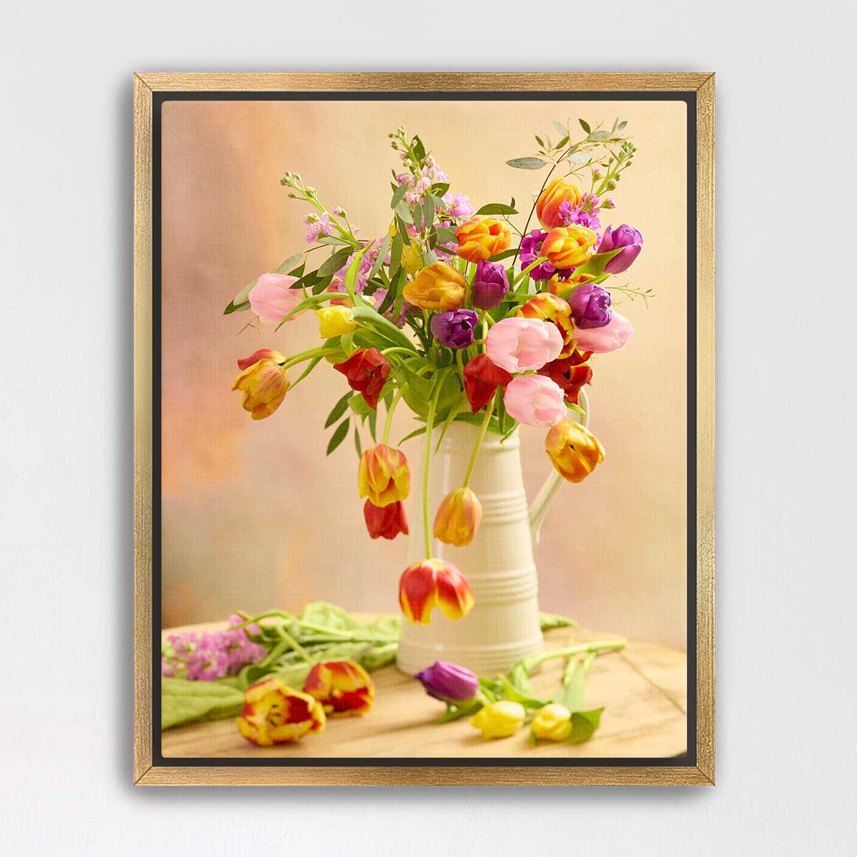 A white vase filled with a vibrant bouquet of tulips in various colors, including pink, yellow, and purple, sits on a wooden surface.