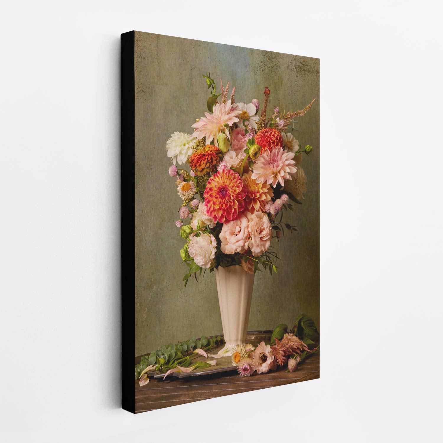 The Victorian Bouquet canvas wall art depicts a still life painting with vibrant dahlias and other flowers in a tall vase, set against an olive-green background on a wooden table adorned with fallen flowers and leaves. This canvas has a wrapped black edge.