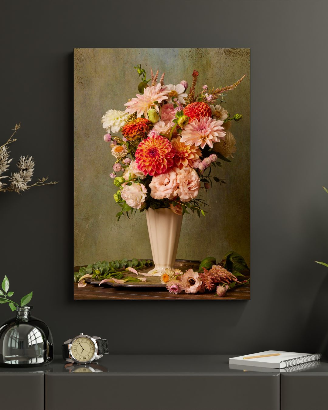 The Victorian Bouquet canvas features vibrant pink and orange dahlias on a dark green wall. Below, a modern table displays a small plant, watch, and closed book, crafting an elegant home decor scene.