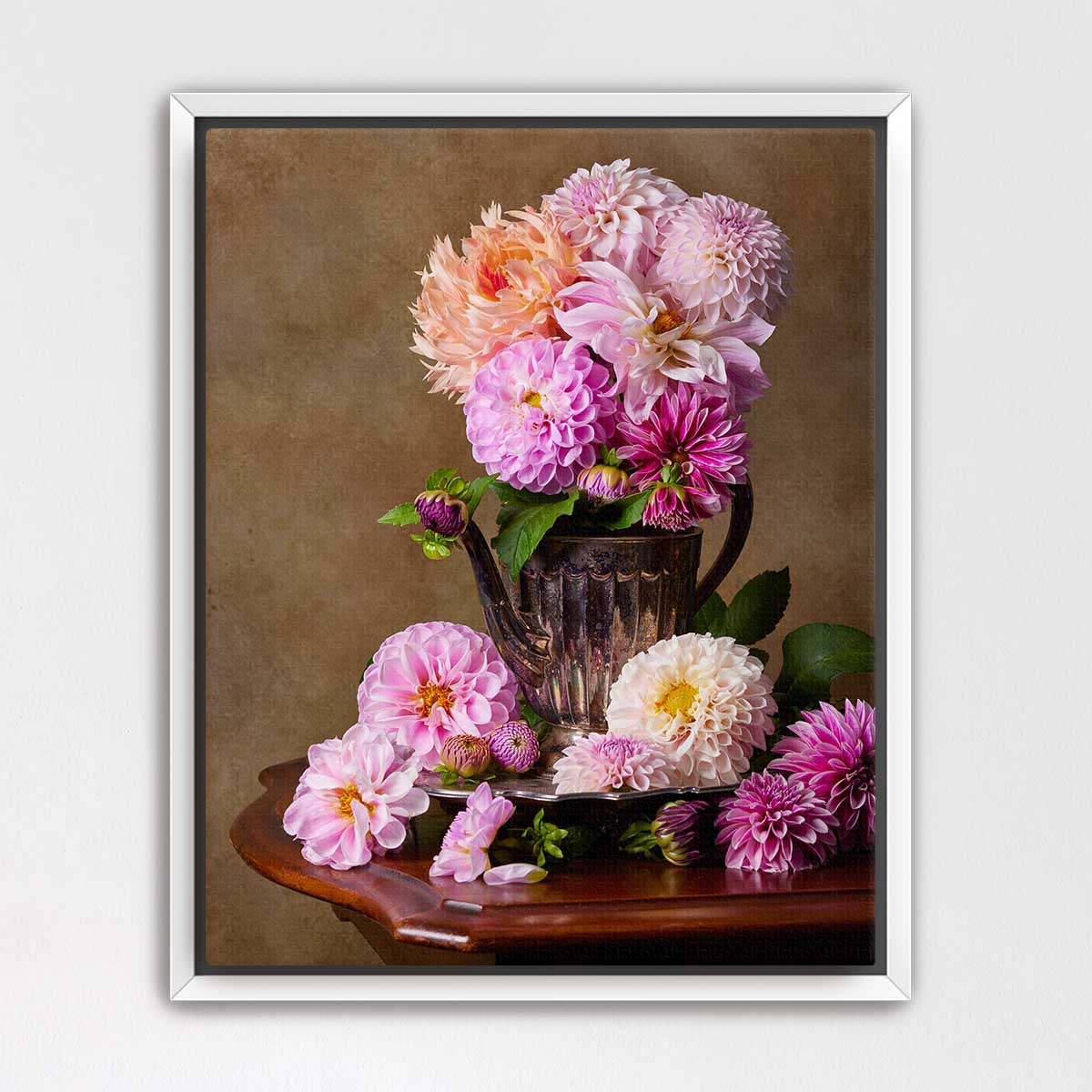 A vase filled with a variety of colorful dahlias sits on a wooden table, surrounded by additional dahlias.