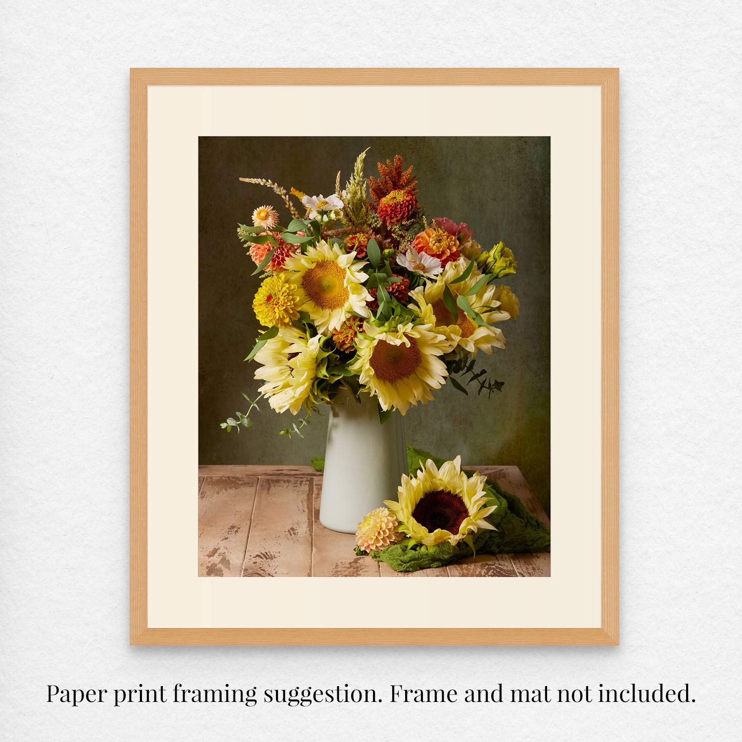 A framed Sunny Bouquet fine art paper print shows vibrant flowers in a vase on a wooden table with a separate sunflower beside it. Text below reads, Paper print framing suggestion. Frame and mat not included.