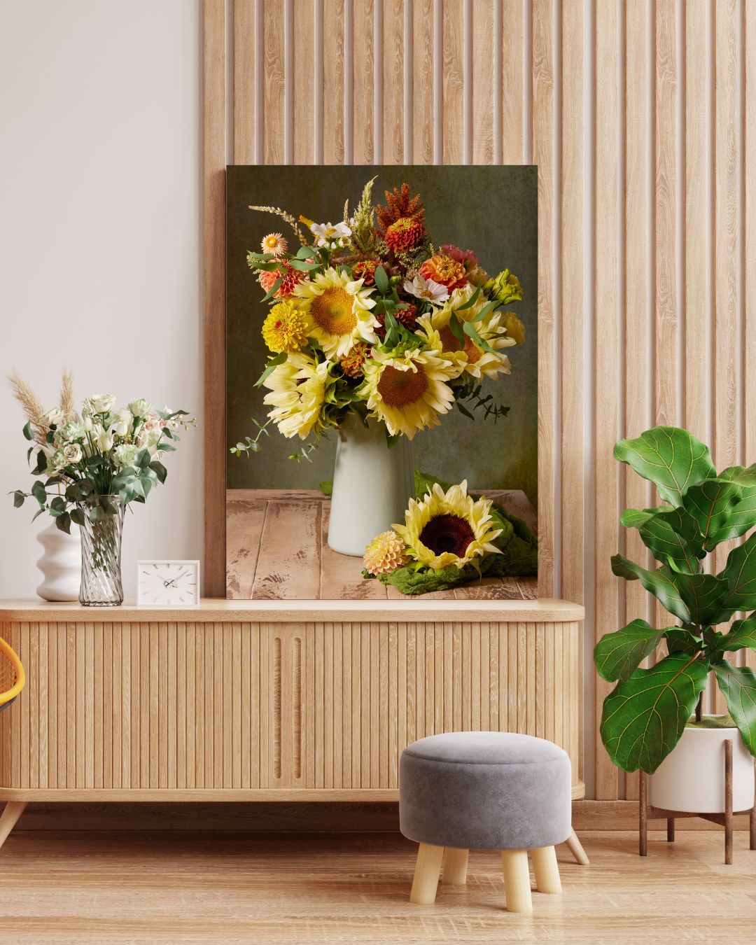 A cozy room showcases the Sunny Bouquet sunflower canvas on a wooden sideboard, complemented by a vase of matching flowers and a plush gray stool. A tall plant in the corner adds greenery.