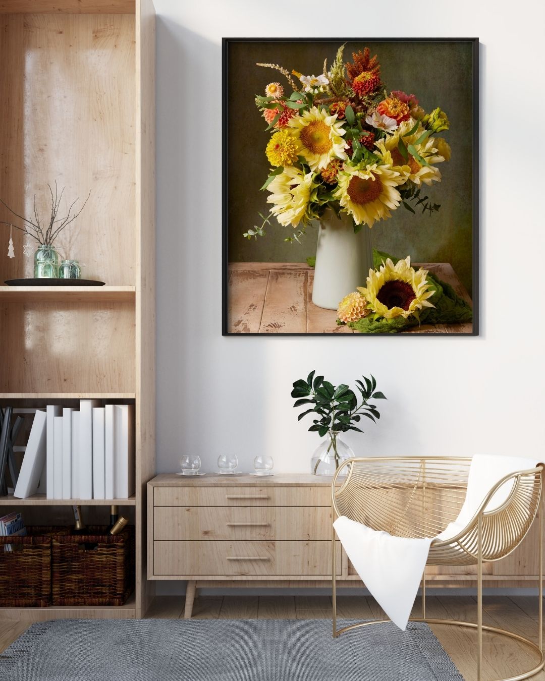 A cozy living room showcases a wicker chair draped with a white blanket, a wooden sideboard adorned with canvas wall art titled Sunny Bouquet depicting sunflowers and other flowers. A vase with a small plant sits on the sideboard beside neatly arranged books.