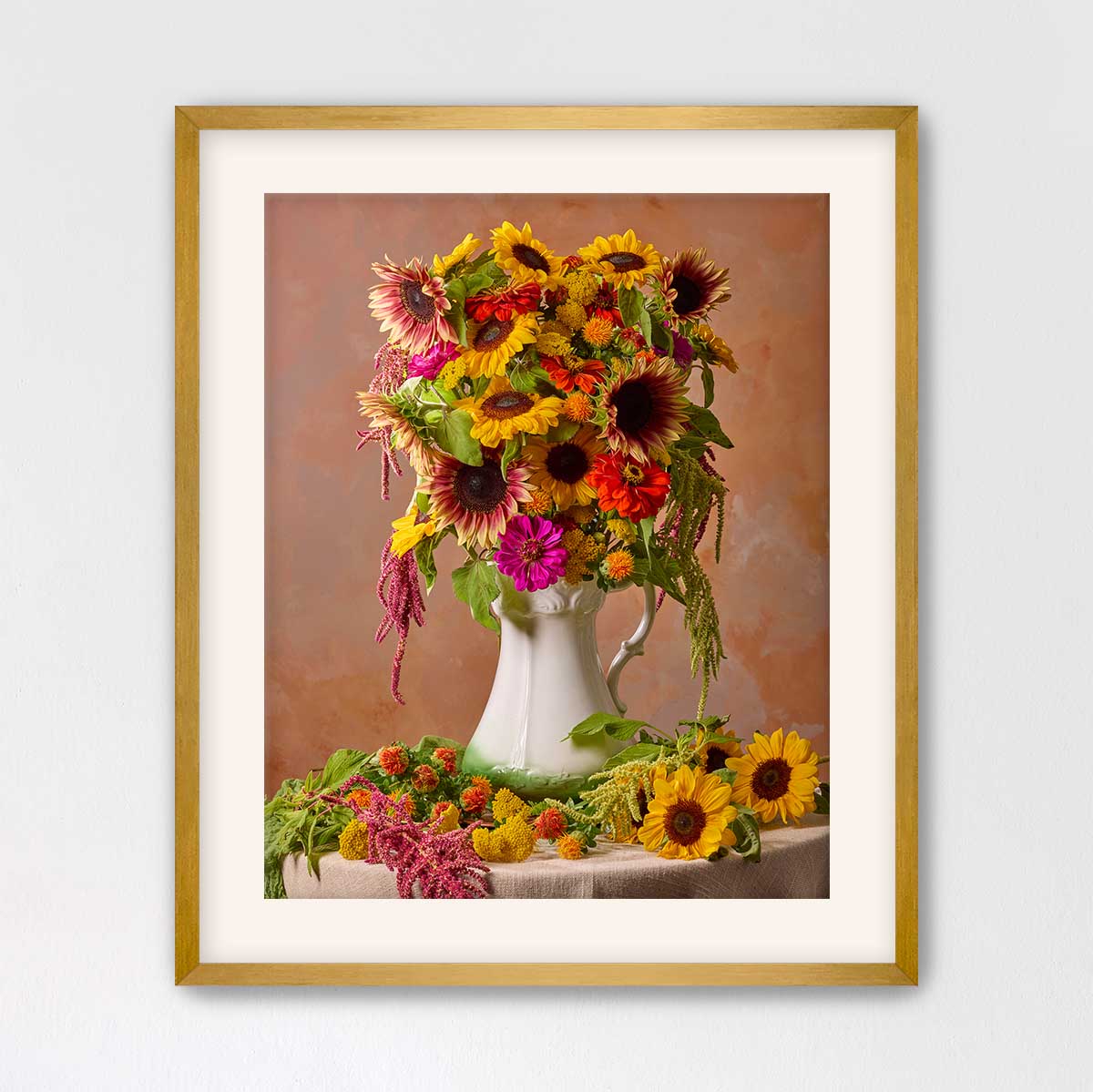 A framed image of a vase filled with a vibrant bouquet of sunflowers and other flowers, set against a warm, peach-colored background.