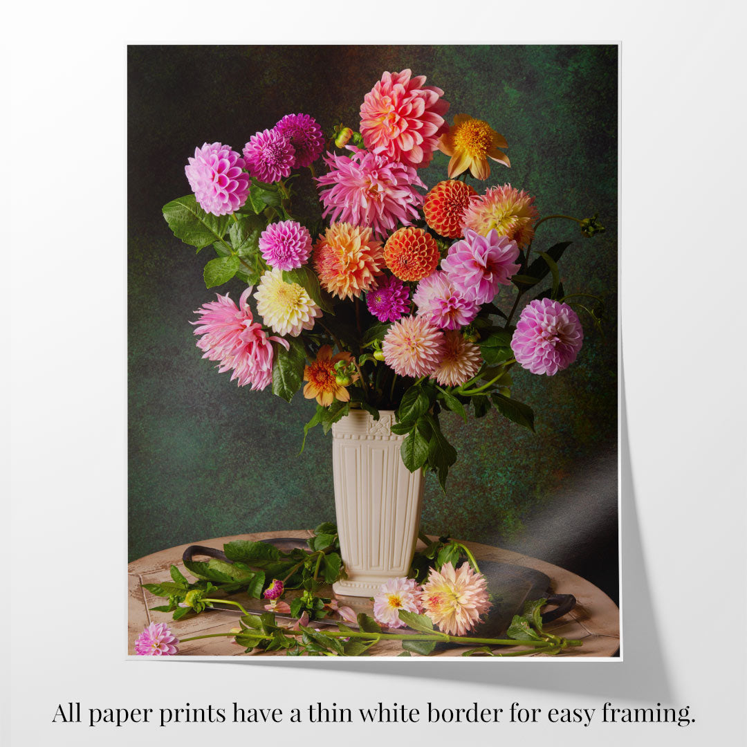 A vibrant mix of pink, purple, and orange dahlias in a cream vase on a dark green background, with scattered dahlias and leaves. Text: Gardens Grand Finale fine art paper prints include a thin white border for easy framing.