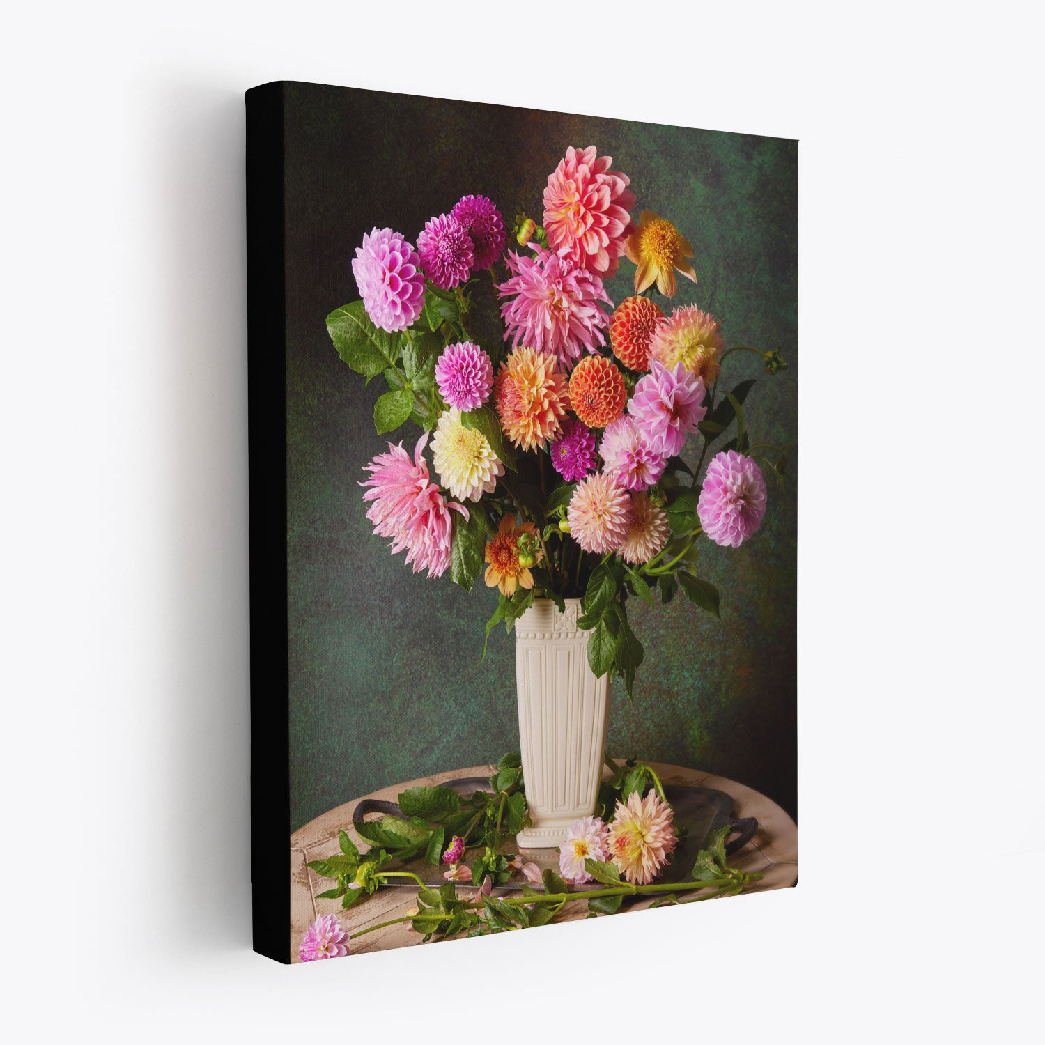 Garden's Grand Finale is a canvas wall art piece featuring a still life of vivid pink, purple, and yellow dahlias in a white vase with textured green background. Flower petals and leaves are tastefully scattered at the base on a wooden surface. This is showing the wrapped canvas has a black edge.