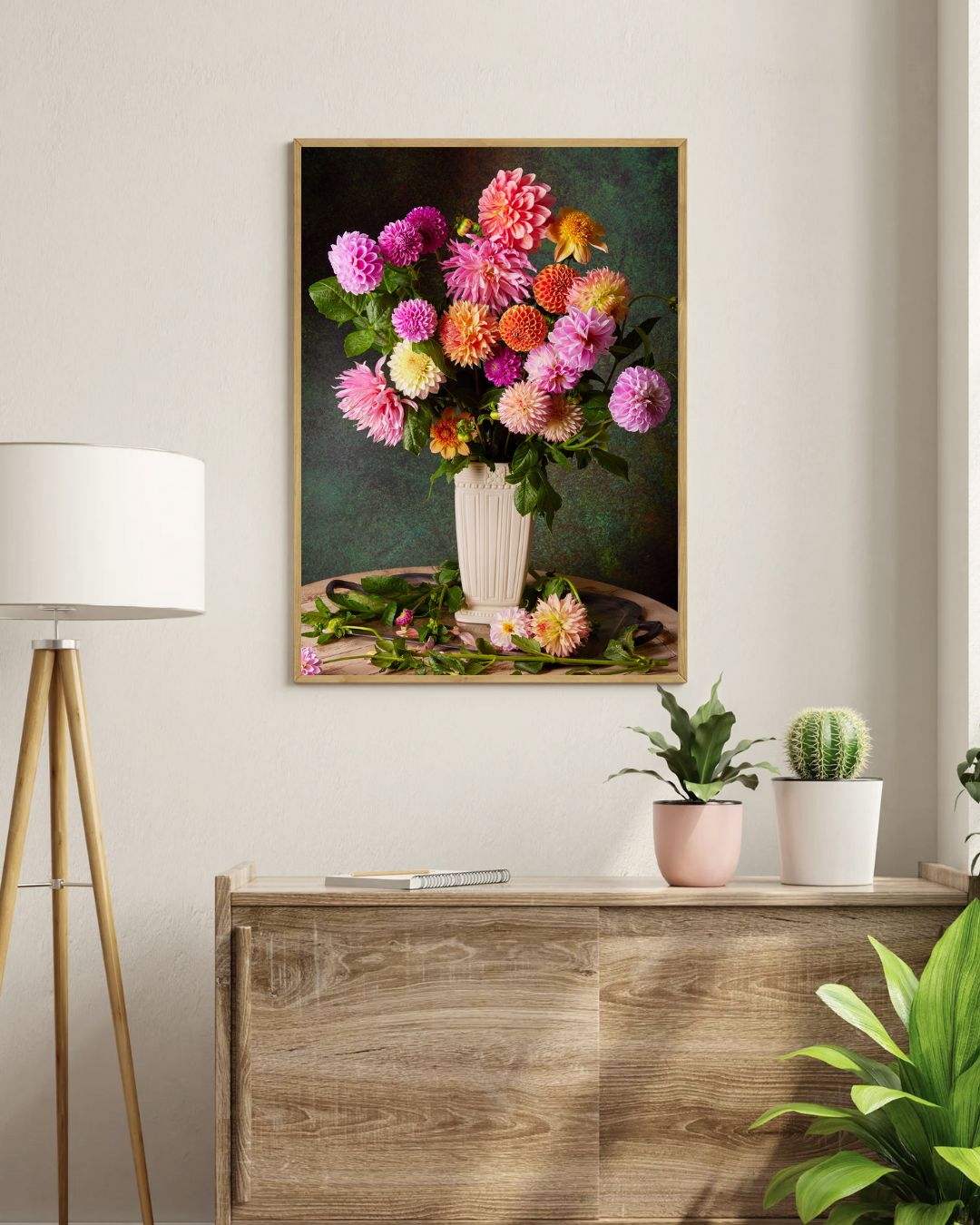 A living room showcases an elegant wooden cabinet with The Garden's Grand Finale floral canvas art above it. A white lamp with a wooden stand sits on the left, flanked by two small potted plants, one in pink.