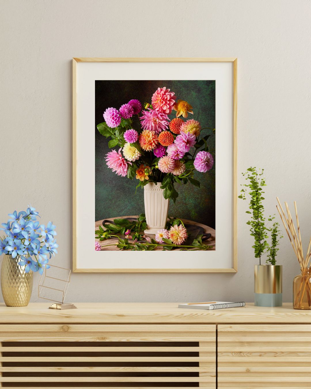 The framed print floral wall art, Garden's Grand Finale, features vibrant flowers in a vase and adorns a wooden cabinet. The cabinet is styled with a small blue floral bouquet and a glass jar of reeds, crafting an elegant fusion of natural beauty and art.