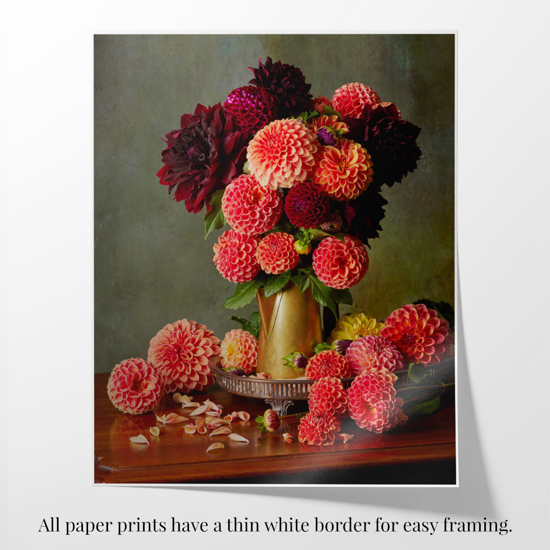 The fine art print Late Summer Glow showcases a still life of red and pink dahlias in a brass coffee pot on a wooden table, with scattered petals. It features a thin white border for easy framing.