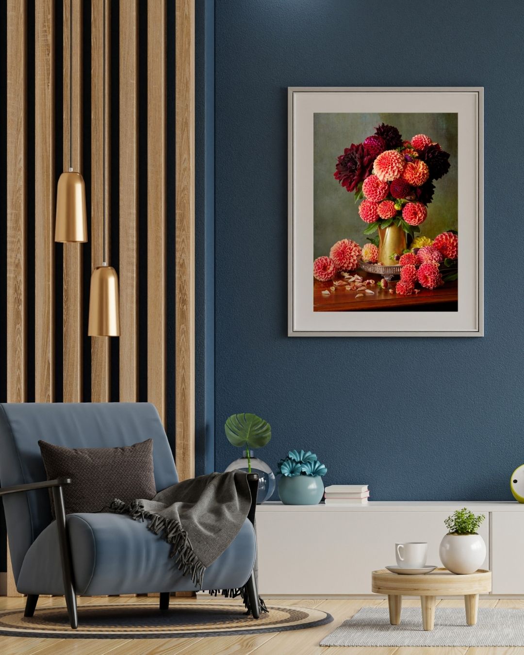 A modern living room features a blue chair with a gray pillow and throw blanket under gold pendant lamps. Late Summer Glow framed canvas art of colorful dahlias adorns the wall, while decorative items and plants sit on the blue shelf below.