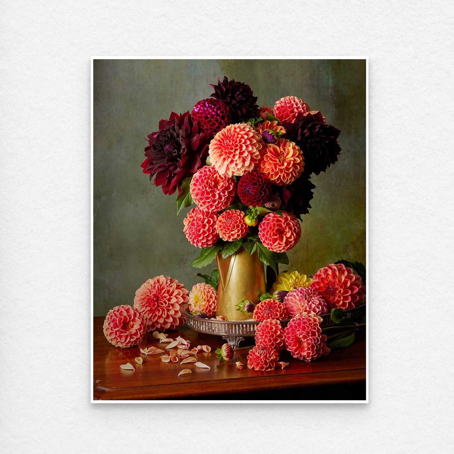 The Late Summer Glow features a vibrant dahlia arrangement in red, orange, and burgundy in a brass coffee pot on a wooden table with scattered petals. This image is showing the paper print with a thin white border for easy framing.