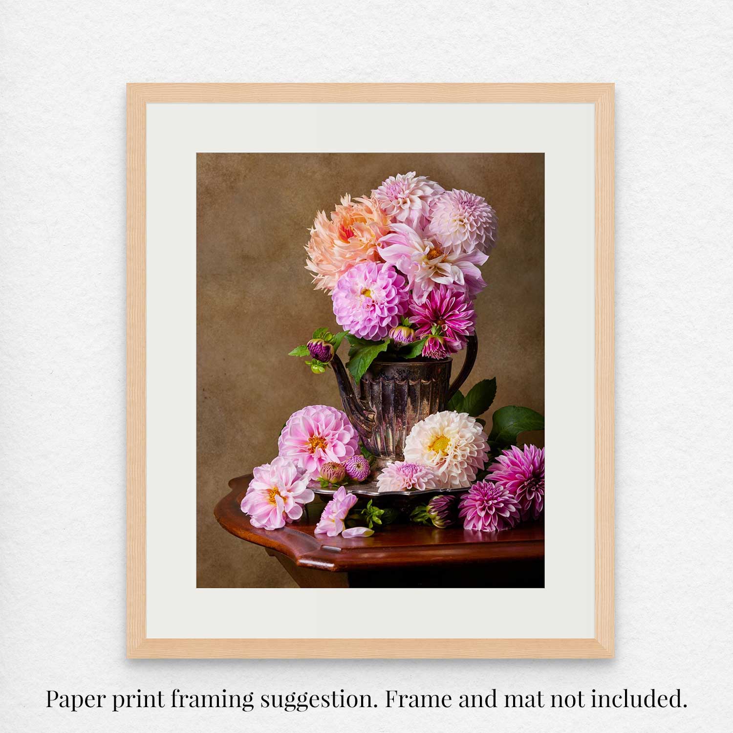 The Dahlia Tea Party as a framed paper print featuring a delightful pink and white dahlia arrangement in an antique silver teapot on a wooden table, set against a muted brown background. Frame and mat are not included.