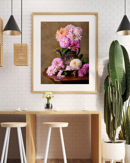 A cozy kitchen nook has a wooden breakfast bar with two white stools, a framed print of the Dahlia Tea Party on the white brick wall,  Pendant lights and leafy plants add a natural touch to this modern, inviting space.