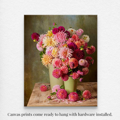 The Dahlia Harvest canvas print features a vibrant array of pink, red, and yellow dahlias in green pots on a textured dark green background. Text below states, Canvas prints come ready to hang with hardware installed.