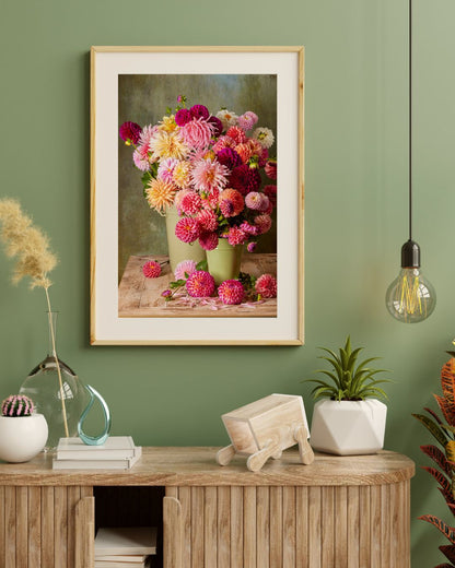 A cozy interior features a framed paper print titled The Dahlia Harvest on a green wall. Below, a wooden console holds books, a glass vase, and potted plants. A pendant light to the right enhances the warm ambiance.