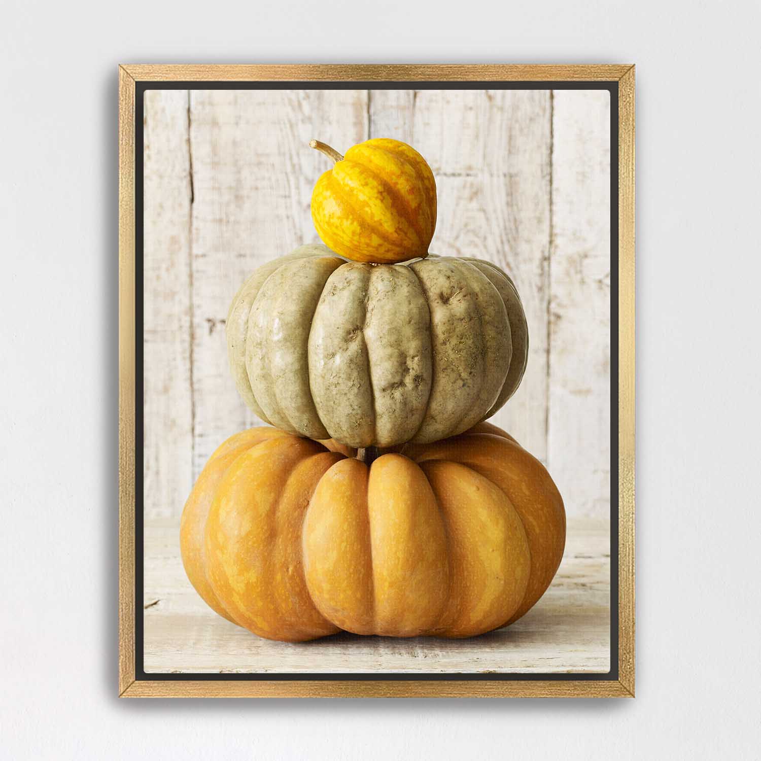 Gold framed artwork of stacked pumpkins on a wooden surface
