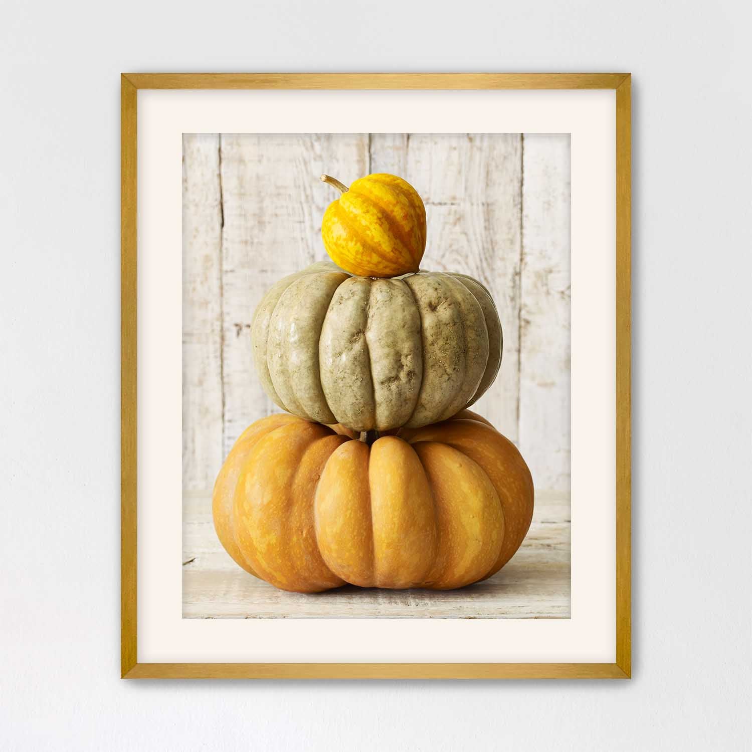 Gold Framed photograph with a cream mat board of stacked pumpkins on a wooden surface