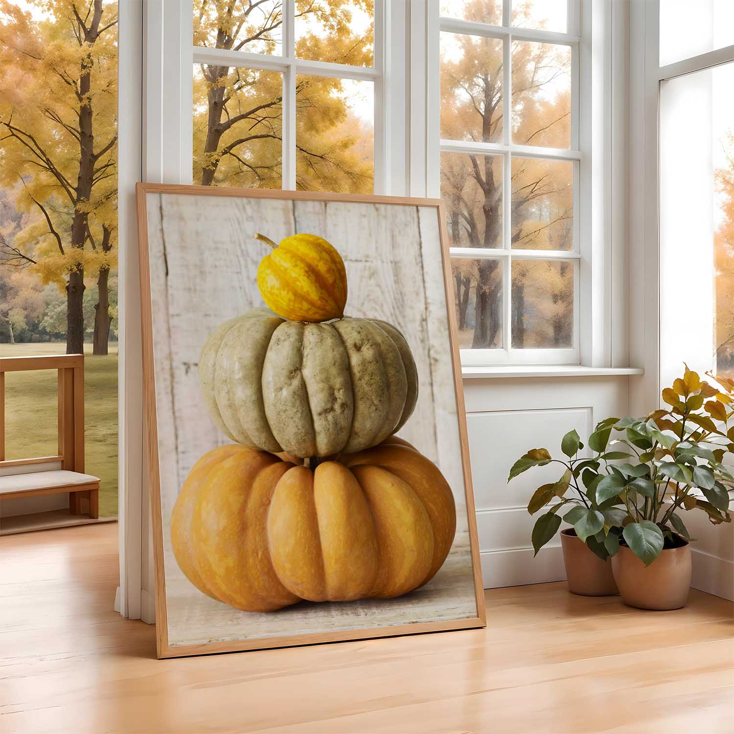 Decorative arrangement of 3 pumpkins in a frame on a wooden floor with a window view of trees.