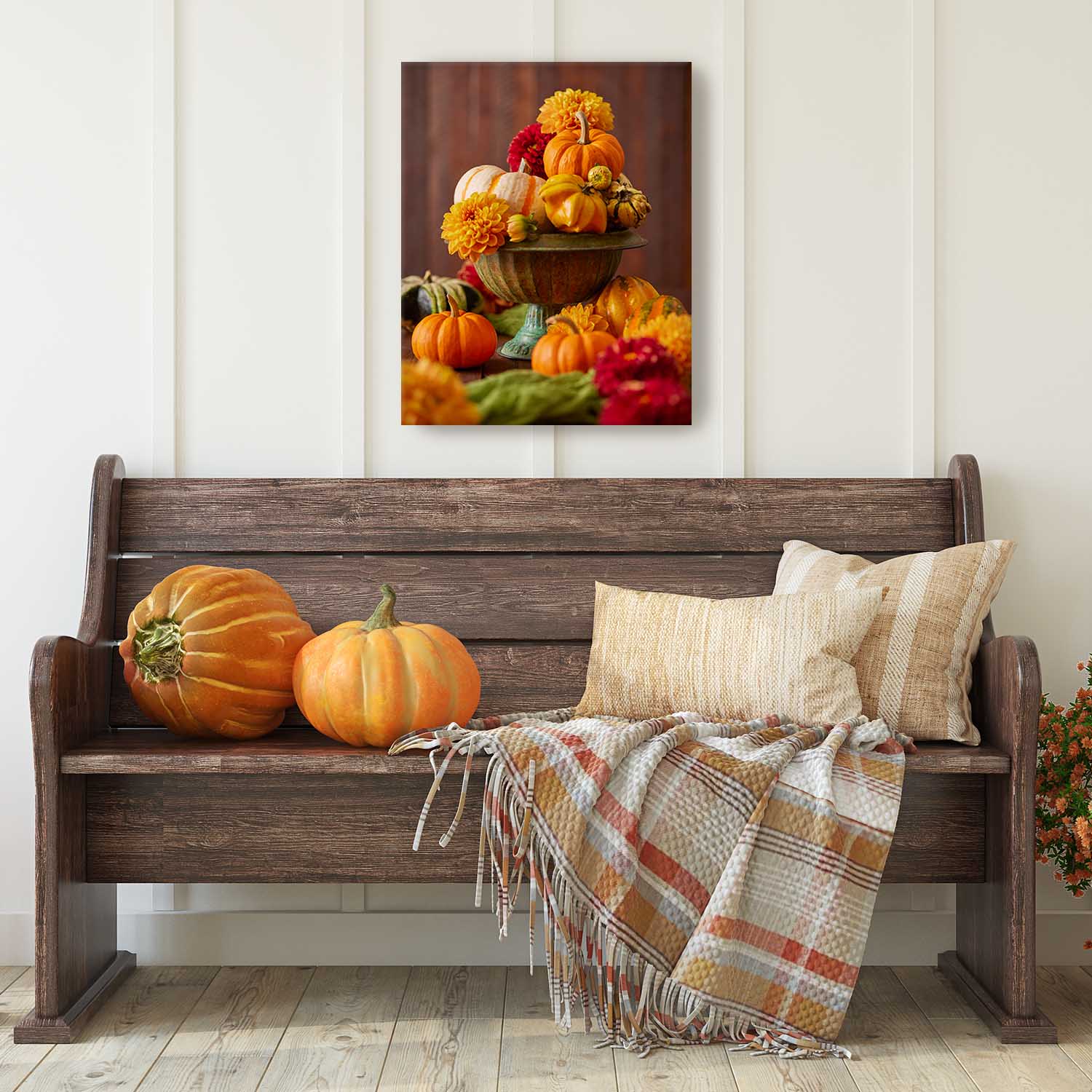 Wooden bench with pumpkins and a plaid blanket, wall art of pumpkins and dahlias above.