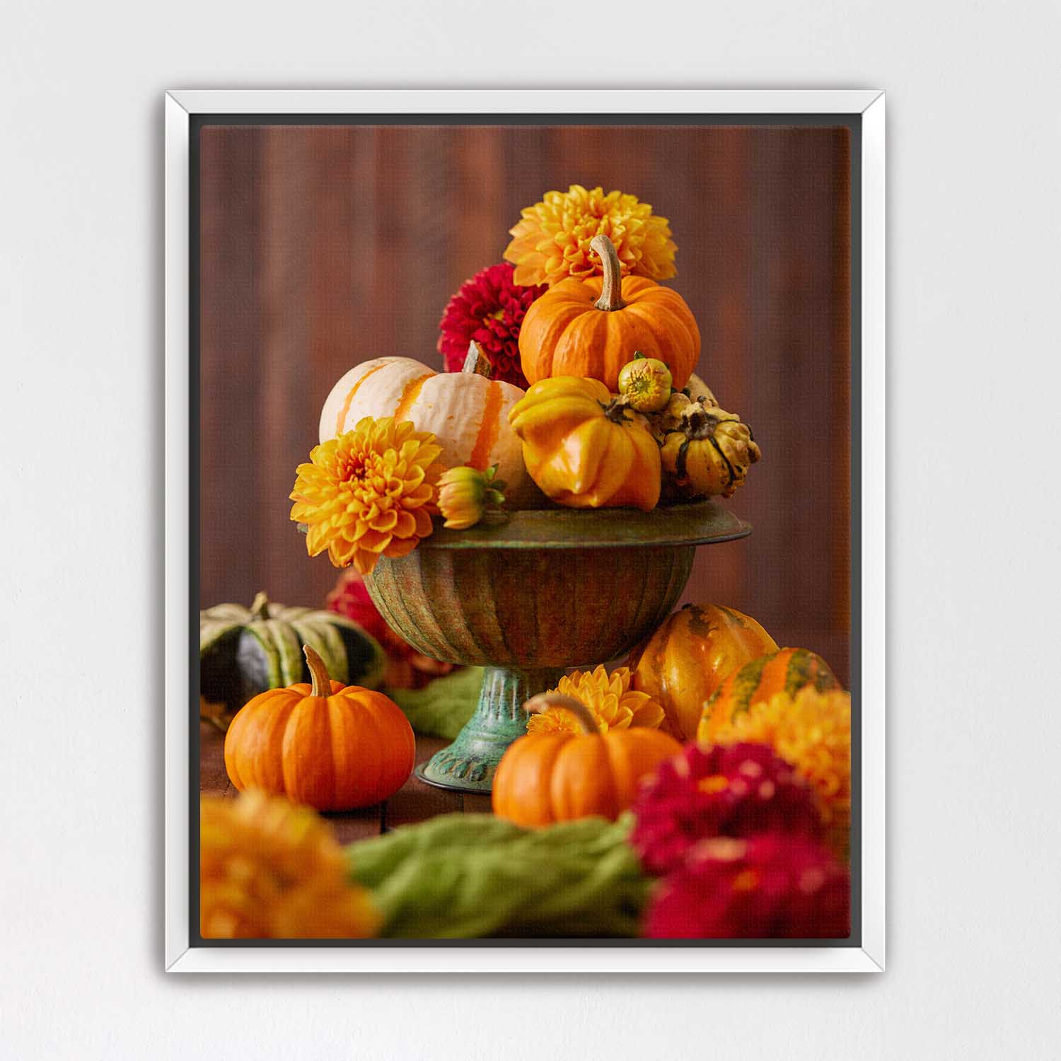 White framed canvas artwork of pumpkins and dahlias on a wooden surface with a brown background