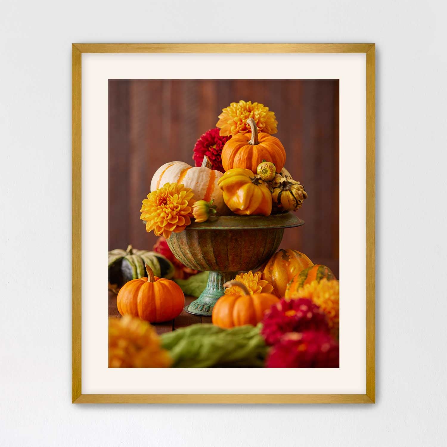 Gold framed print with a cream mat board of a still life arrangement with pumpkins and dahlias on a wooden surface.