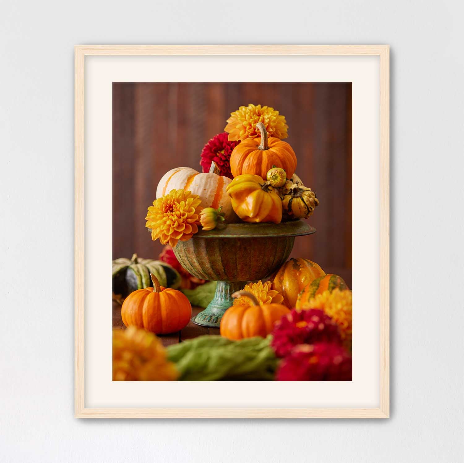 Maple framed still life arrangement with pumpkins, gourds, and dahlias on a wooden surface.