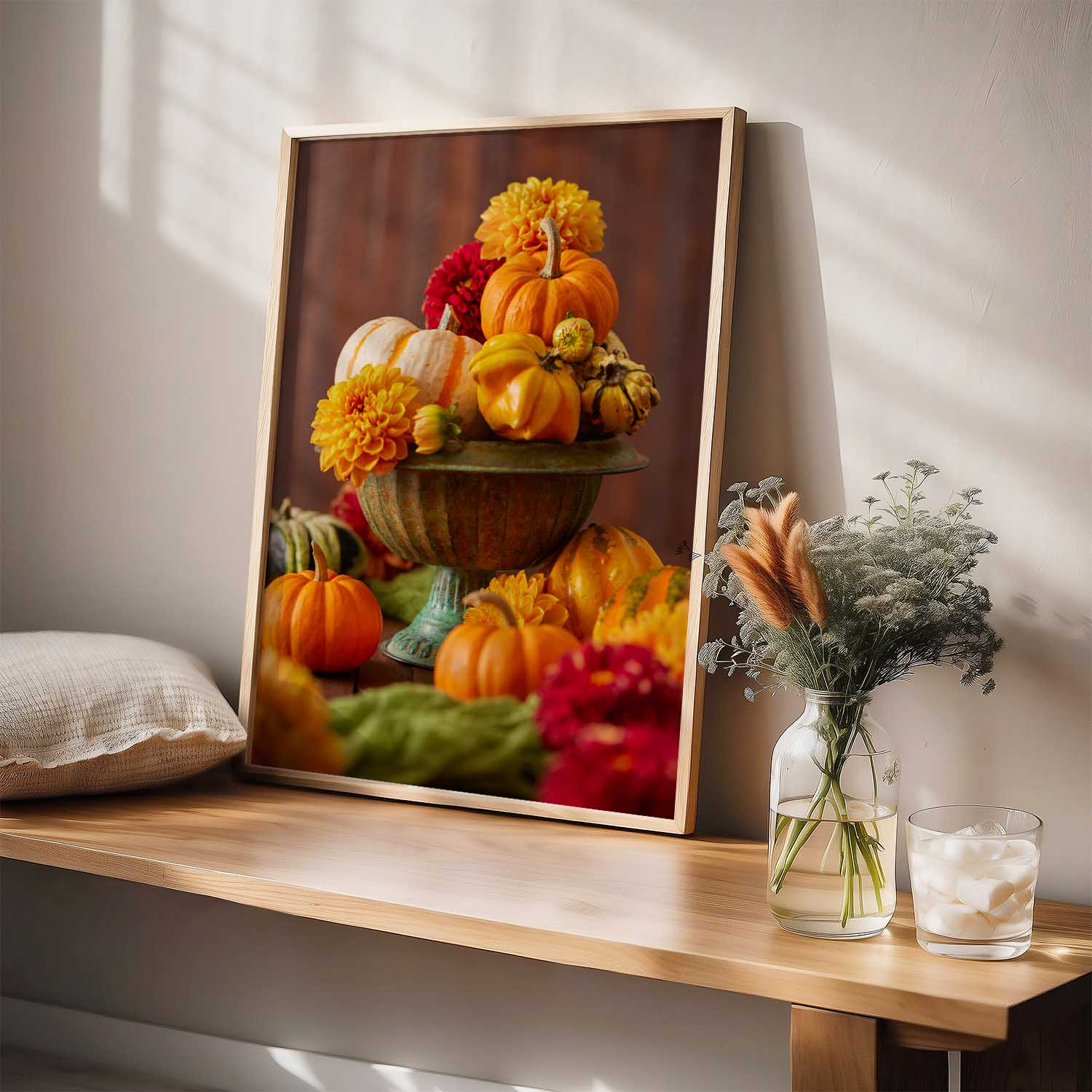 Maple framed canvas of pumpkins and dahlias on a wooden shelf with a vase and glass.