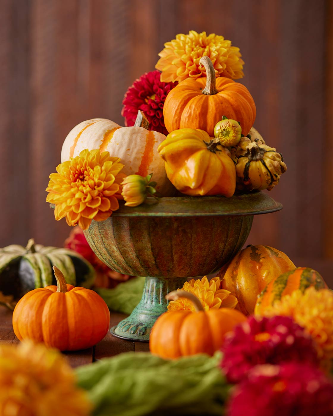 Decorative arrangement of pumpkins and gourds with dahlias on a wooden surface.