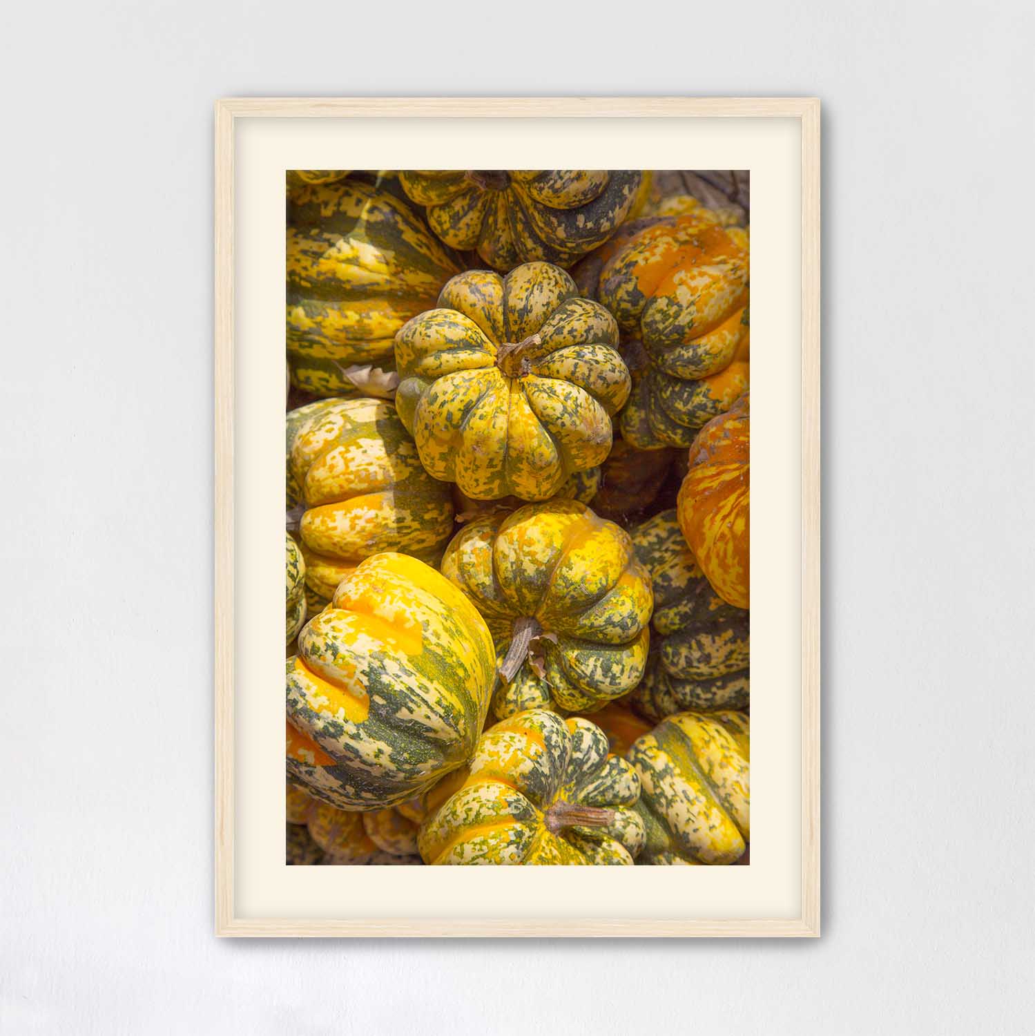 Maple framed photograph of yellow and green pumpkins on a light gray wall