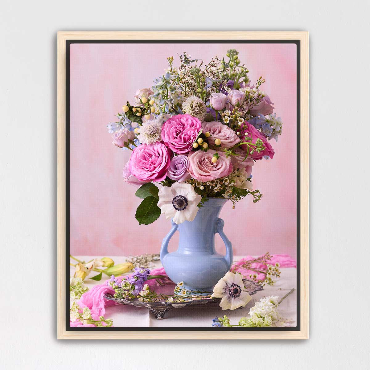 A framed image of a vase filled with a vibrant bouquet of pink roses, white anemones, and other colorful flowers against a pink background.