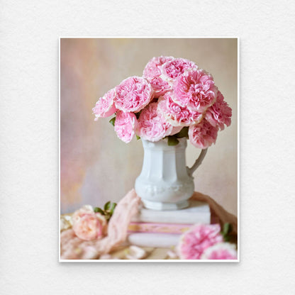 Paper print with a white border showing a white ceramic pitcher with a bouquet of Miranda roses sits atop a stack of books, set against a pastel-toned background.