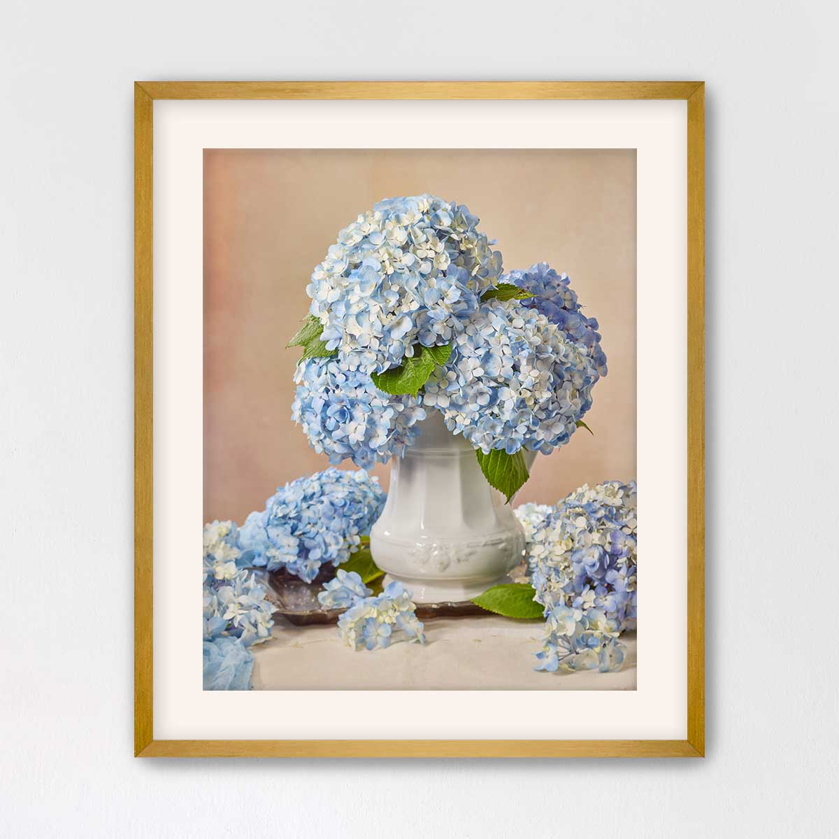 A framed photograph of a white vase filled with blue hydrangea flowers, placed on a table.