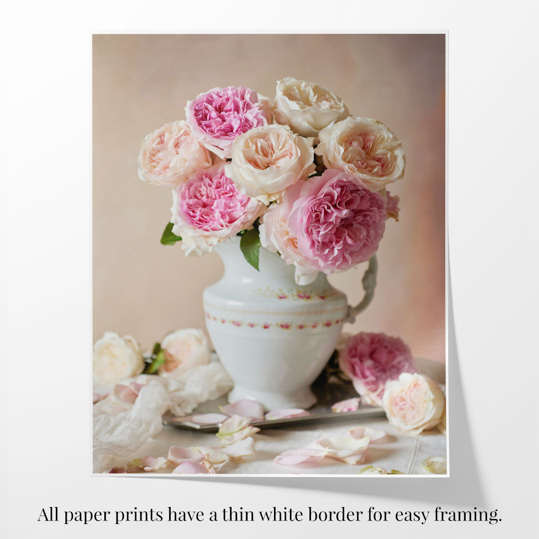 The Romance in Bloom print features a white ceramic vase with pink and white David Austin roses on a table, surrounded by scattered petals. All prints come with a thin white border for easy framing.