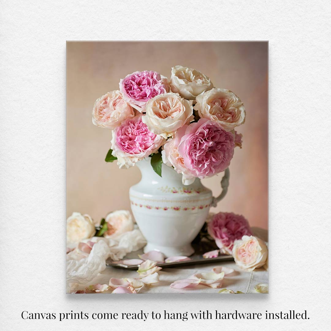 Romance in Bloom canvas wall art features pink and cream David Austin roses in a white vase on a light surface, with scattered petals and blooms. Comes ready to hang with hardware installed.