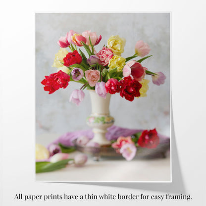 The image titled Spring Symphony showcases a vase of vibrant red, pink, and yellow tulips, with softly focused scattered petals. It features a thin white border for easy framing.