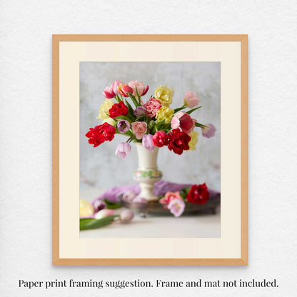 The Spring Symphony print presents a lively floral arrangement featuring red, yellow, and pink tulips in a white vase, set against a soft, blurred background enhancing its springtime charm. Note: Its a paper print; frame and mat not included.