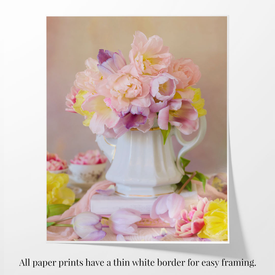 Teapot of Blooms has a white pitcher holding pink and yellow spring tulips on a pastel surface. Soft focus flowers surround, crafting a dreamy feel. Below, text indicates that all fine art prints feature a thin white border for easy framing.