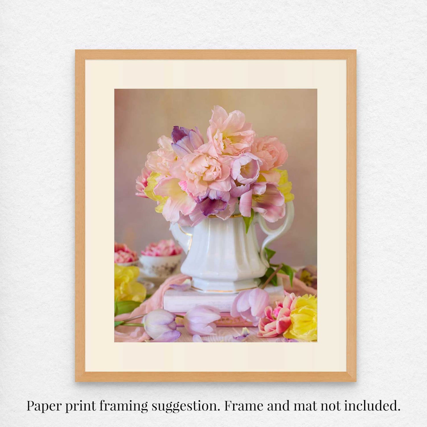 Teapot of Blooms is a fine art print featuring pink and yellow tulips in a white vase, embodying the essence of spring. A blurred background with soft pastel colors complements this piece. Text below reads: Paper print framing suggestion. Frame and mat not included.