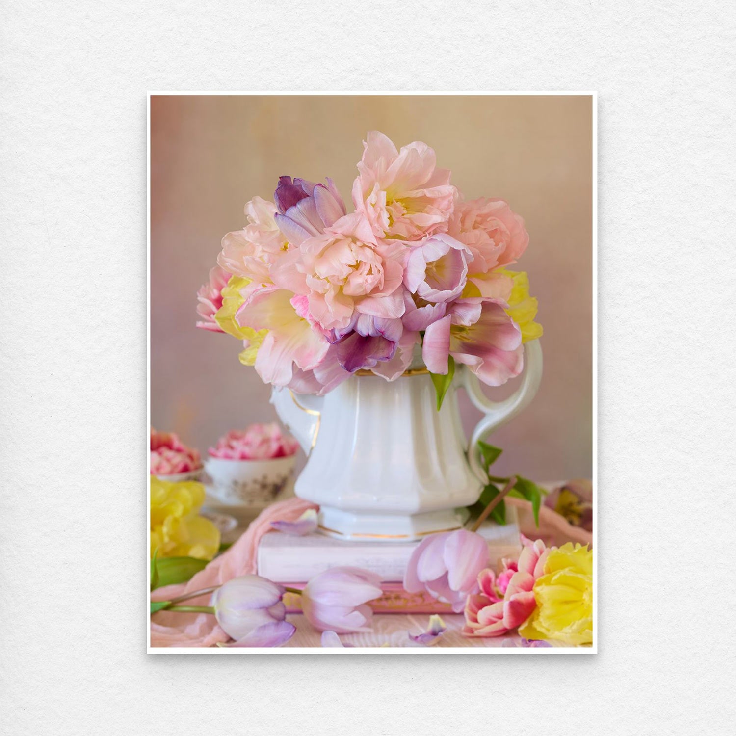 The Teapot of Blooms, a white ceramic container, overflows with pink and purple tulips against a soft backdrop. This paper print is shown with a thin white edge for easy framing.