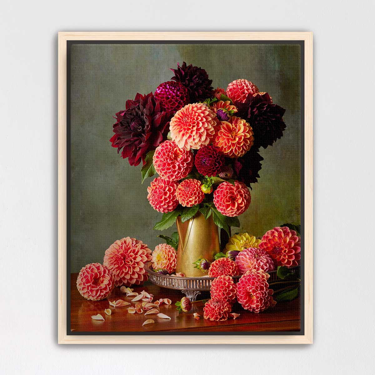 A framed still life painting depicting a vase filled with a variety of colorful dahlias, including red, pink, and yellow flowers, along with some fallen petals on a wooden surface.