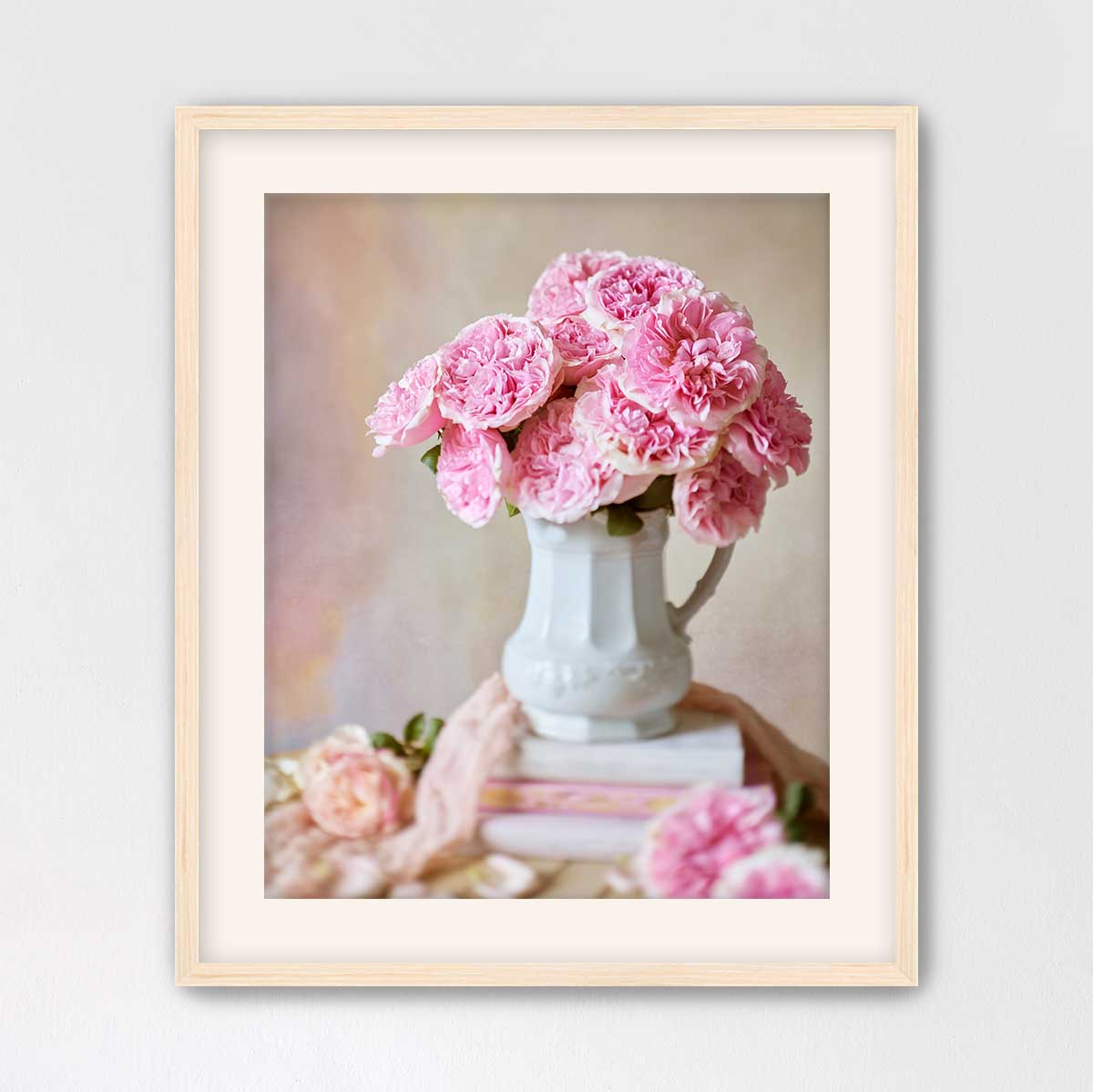 A white vase filled with pink flowers sits on top of a stack of books, creating a charming and elegant still life composition.