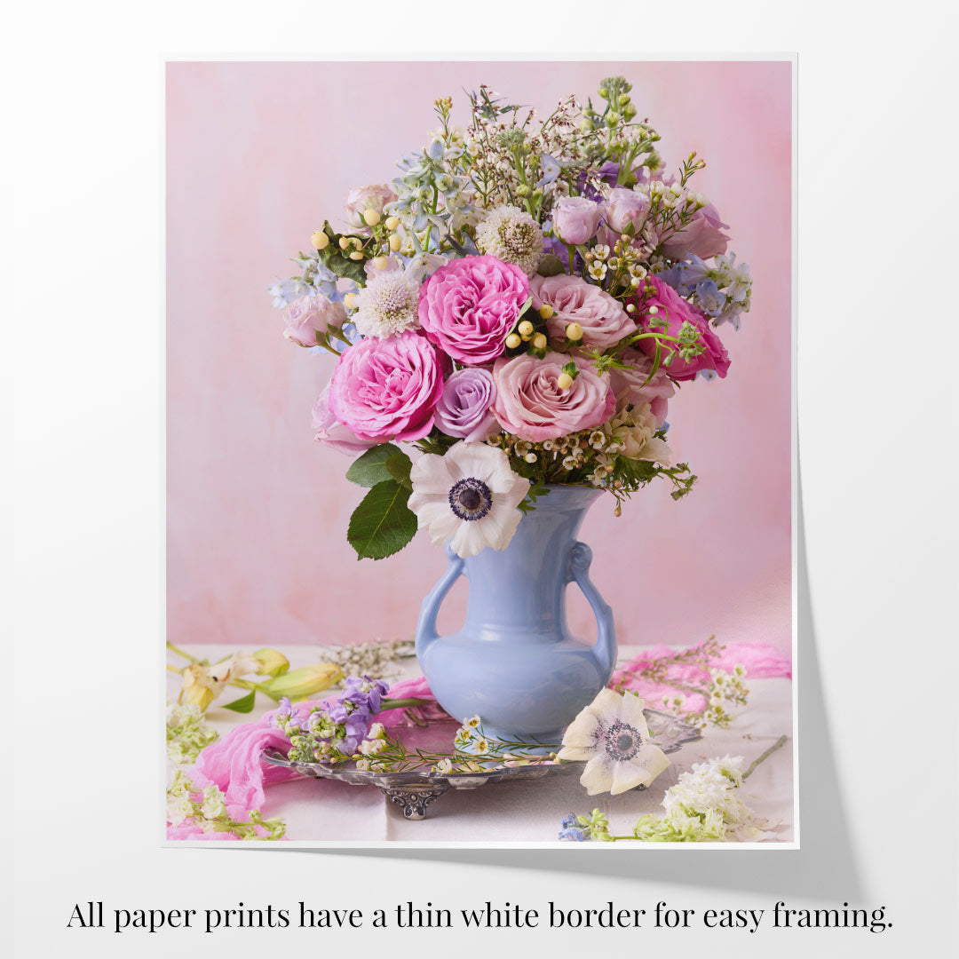 On a table sits the Pink and Blue Serenade, a blue vase floral arrangement with pastel roses and other flowers. Against a soft pink background, the text states all paper prints include a thin white border for easy framing, ideal for modern canvas wall art.