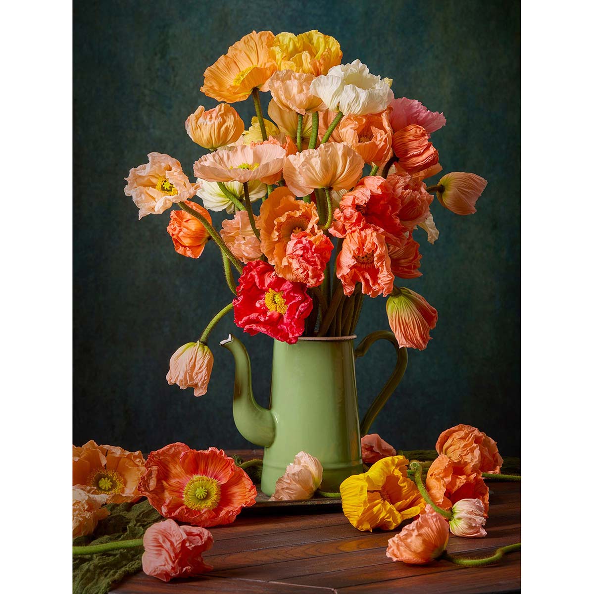 Italian poppies arranged in an antique green teapot on a wooden table with a dark green backdrop
