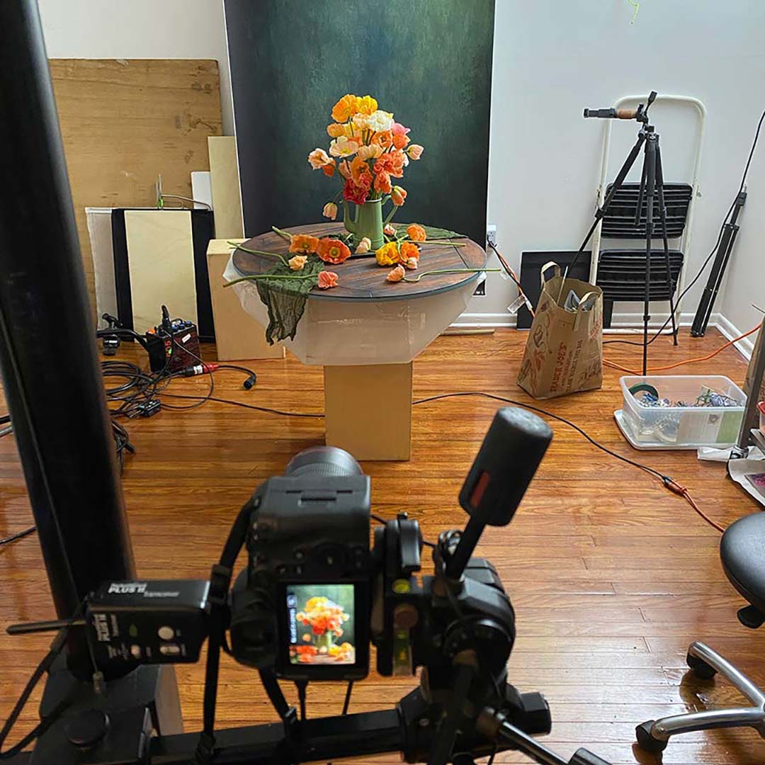Camera setup with the Poppy Passion flower arrangement on a wooden table in a room with various equipment.