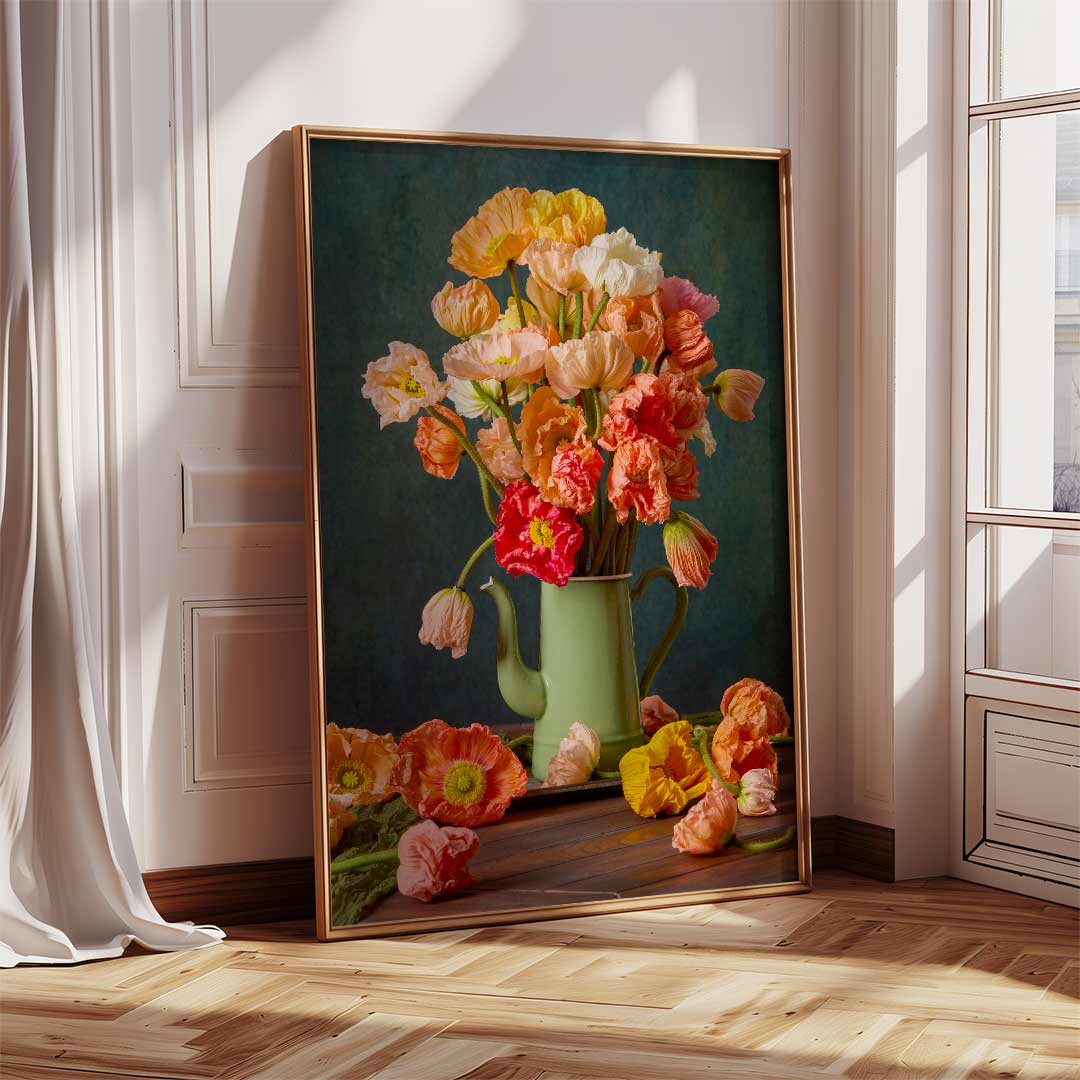 The framed canvas Poppy Passion showcases vibrant orange, pink, and yellow poppies in a green teapot. Frame is leaning against the wall of a sunlit room. Light reflects off the wooden floor while a white curtain is partly visible.